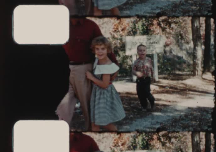 A father and his young daughter walk together through a sunny park in this charming vintage home movie footage from the 1950s