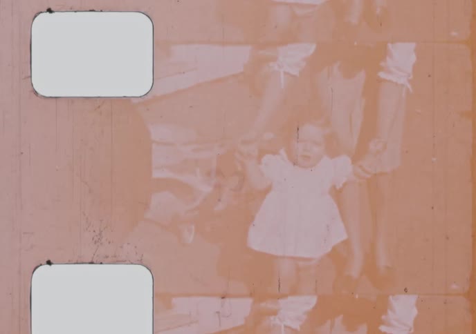 Vintage 8mm home movie footage shows a baby girl sitting and then taking her first steps with her mother's help