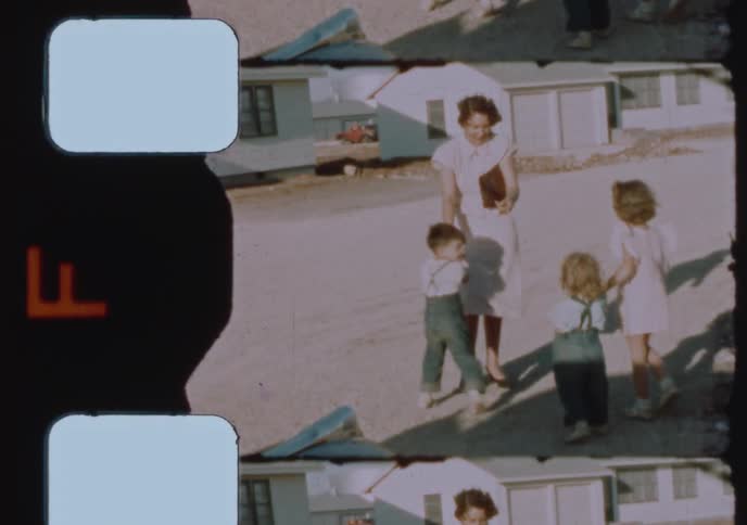 An authentic 1950s home movie captures a happy mother holding hands with her three young children as they walk together outside their suburban home