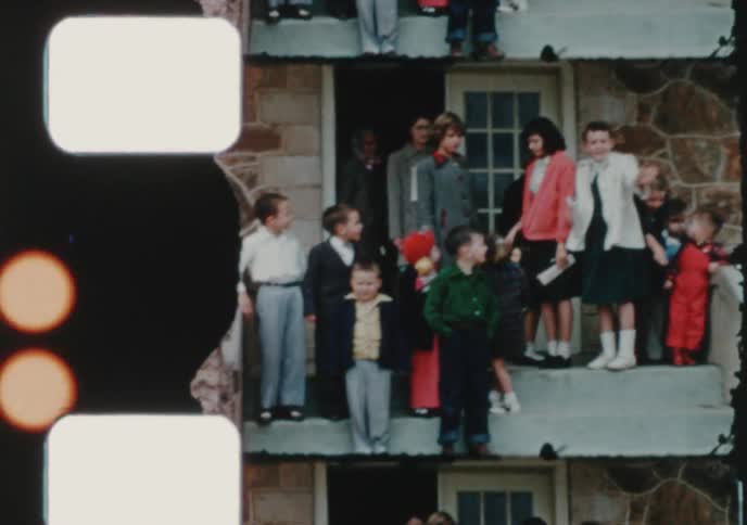 Families and children dressed in their Sunday best gather on the steps of a stone house in this vintage 1950s home movie