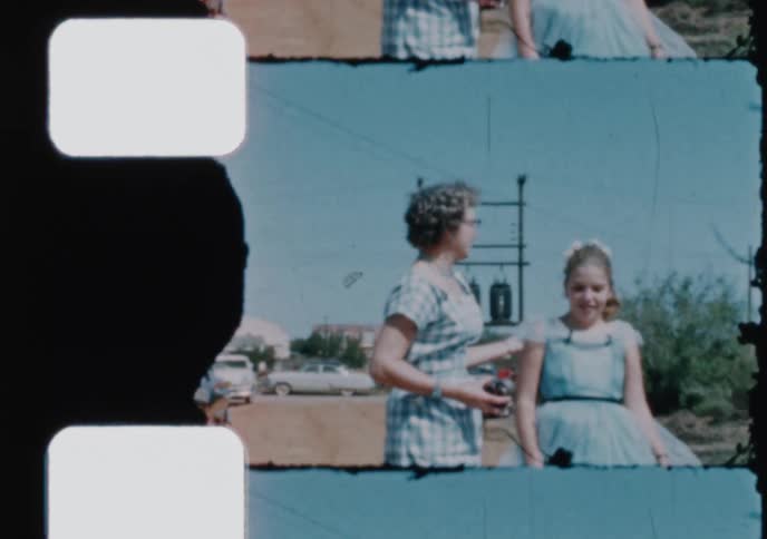 A mother and her two children in their Sunday best walk along a dirt road in this scanned 1950s home movie