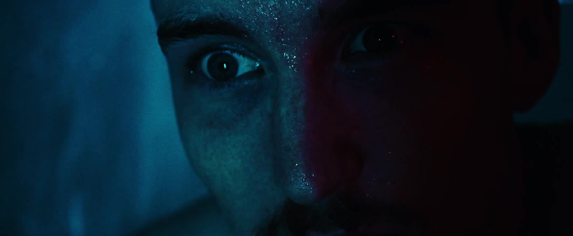 Extreme close-up on the intense, sweaty face of a man staring with wide eyes under dramatic blue lighting