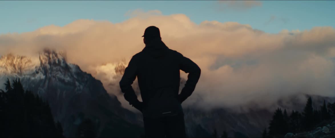 An athletic man pauses during his morning run to admire the majestic, cloud-covered mountains at sunrise