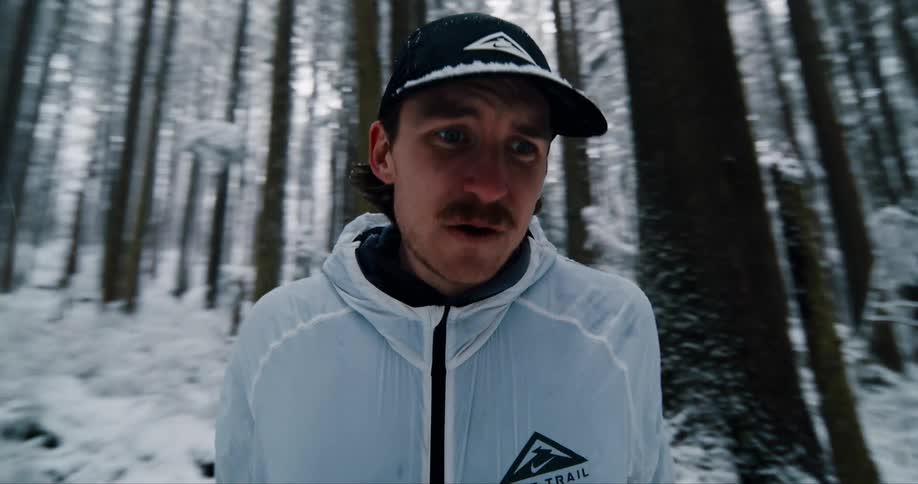 A determined athlete catches his breath while trail running through a dizzying, snow-covered forest