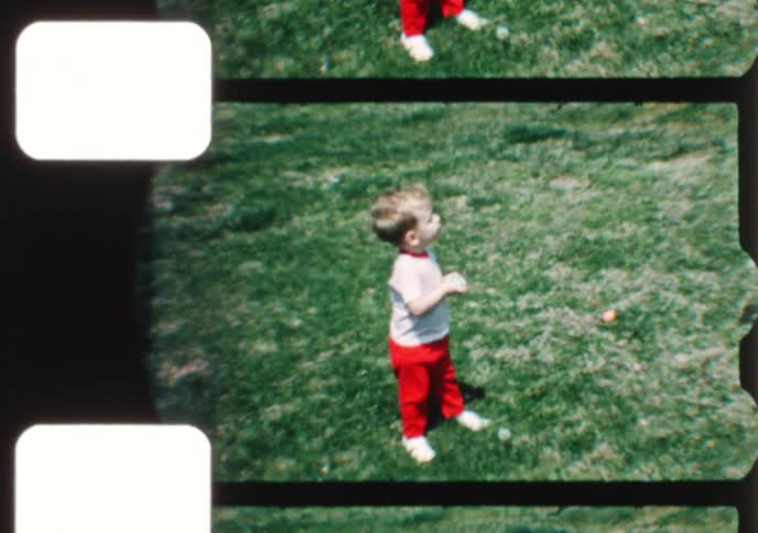 An adorable toddler collects colorful eggs during an Easter egg hunt with his mother in their backyard in this charming vintage home movie