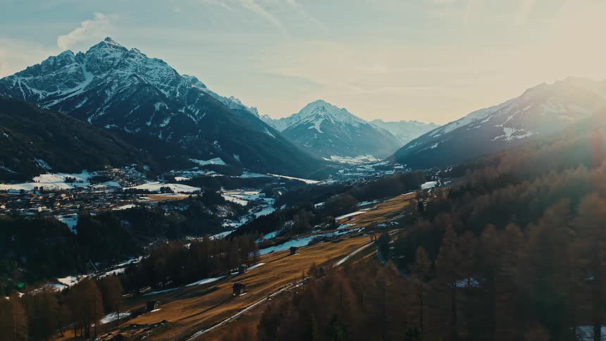 A serene mountain valley awakens as the morning sun casts its golden light over snow-capped peaks and a tranquil town below