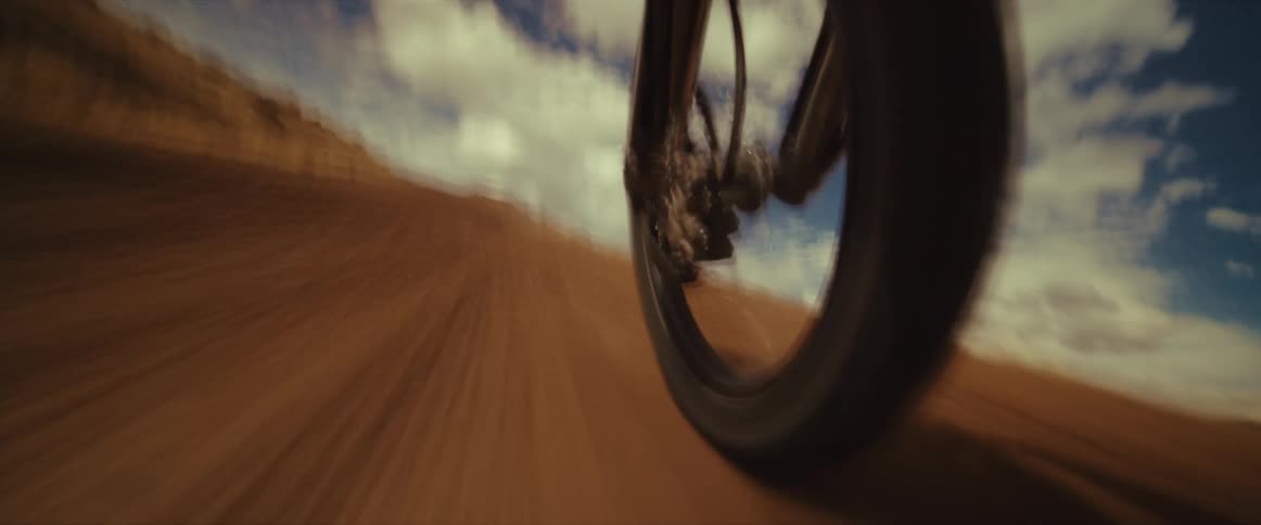 A dramatic low-angle shot of a motorcycle's front wheel spinning quickly on a dusty desert road