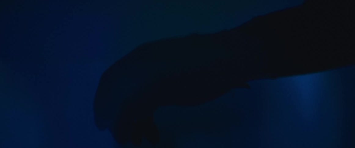 An abstract shot shows a shadowy hand moving through a hazy, deep blue environment