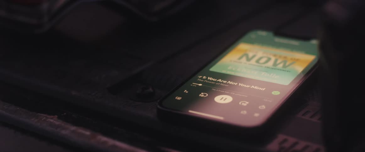A close-up shot of a smartphone playing the audiobook 'The Power of Now' by Eckhart Tolle in a dimly lit room