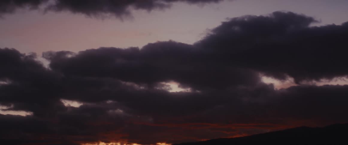 Dark clouds fill the sky at dusk, with faint hints of red and orange from the setting sun on the horizon