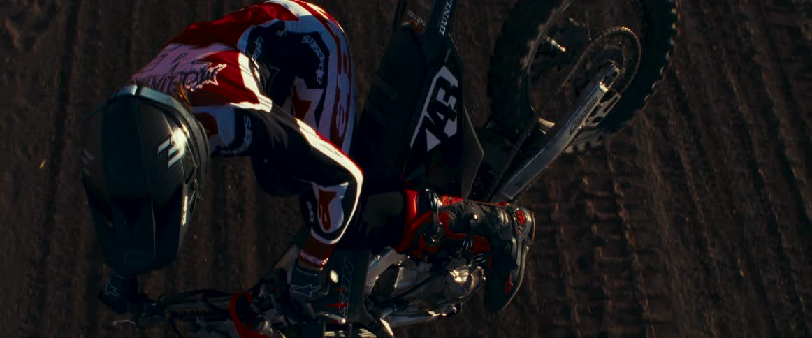 A professional motocross racer performs a jump in midair in slow motion at sunset on a dirt track