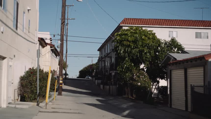 A slow zoom down a sun-drenched, empty residential alleyway leading uphill on a bright day