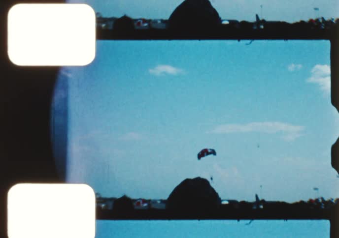 Archival 8mm film captures various scenes from an airshow, including parachutists, a control tower, and military fighter jets on the runway