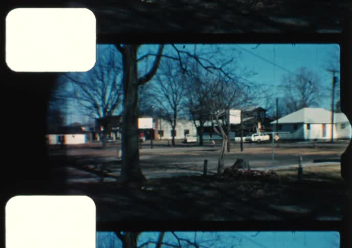 An 8mm home movie captures a quiet suburban neighborhood with a classic car parked in front of a house on a clear day