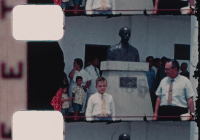 A father and son stand by a statue in a town square in this vintage home movie footage