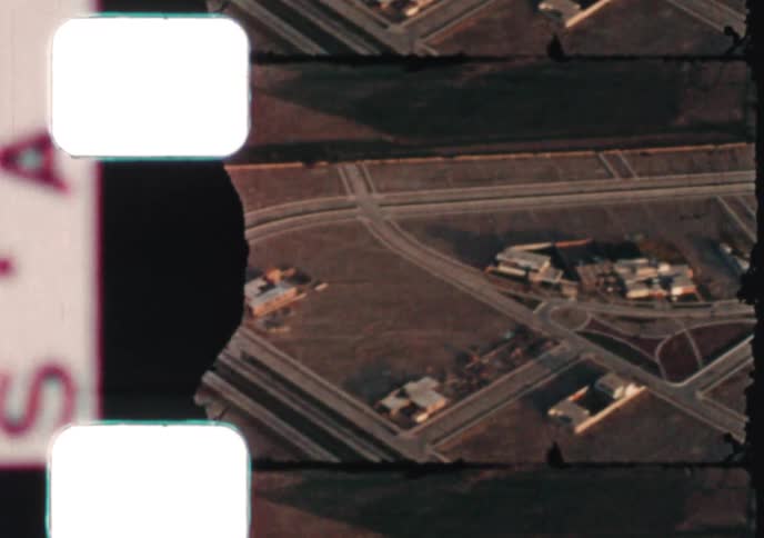 An aerial view from damaged vintage film shows a desert landscape with a growing suburban community