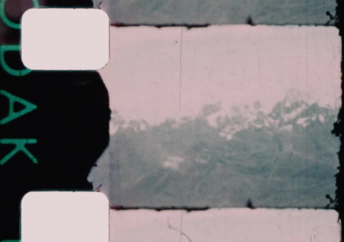 A vintage 8mm film from 1960 captures a majestic aerial view of a snow-capped mountain range from an airplane window