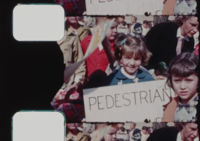 Vintage 16mm film shows a small town American parade with a marching band and a young girl holding a 'Pedestrian of the Week' sign
