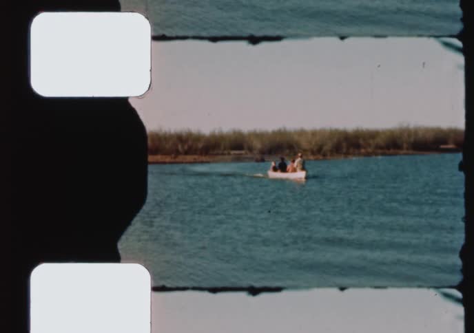 A family in a small motorboat enjoys a leisurely ride across a calm lake in this vintage 8mm home movie