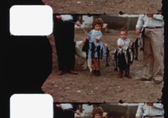 Two young children proudly show off their strings of freshly caught fish with their family in this vintage 16mm home movie
