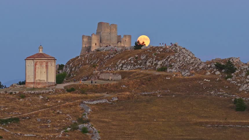 A giant full moon rises over the ancient Rocca Calascio castle in Abruzzo, Italy, as people watch from the hilltop at dusk