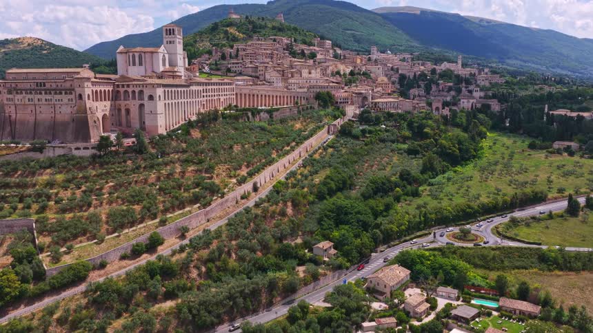 Sweeping aerial footage reveals the historic Basilica of Saint Francis and the town of Assisi, Italy, set against the lush green hills of Umbria