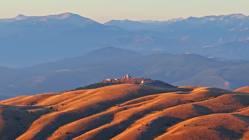 Golden sunrise light illuminates the rolling hills and the distant ancient fortress of Rocca Calascio in the Italian Apennine Mountains