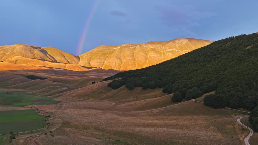 A stunning aerial view of a vibrant rainbow arching over a majestic mountain range bathed in the warm glow of sunset