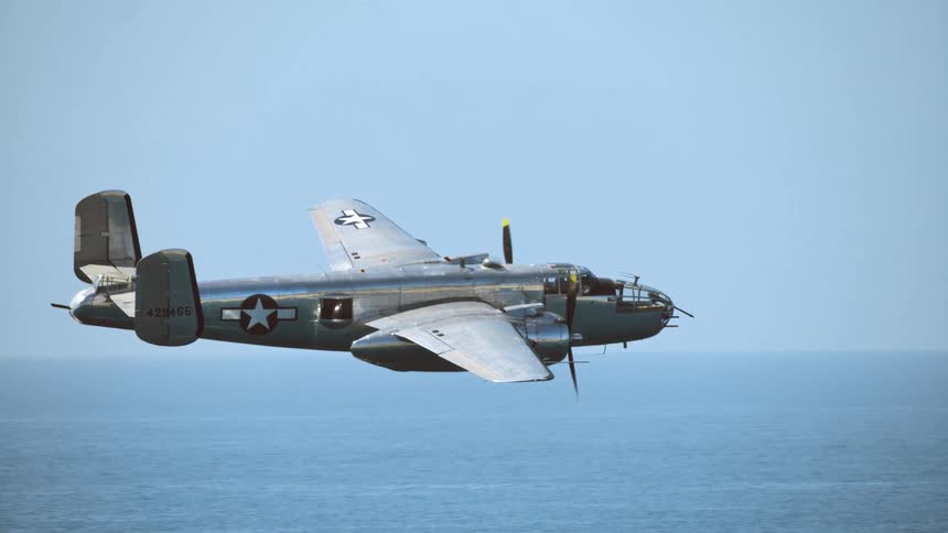 A classic B-25 Mitchell bomber from World War II flies in slow motion over the open ocean on a clear day