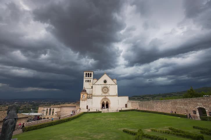A dramatic dolly-out timelapse reveals the Basilica of Saint Francis of Assisi as ominous storm clouds gather overhead in Italy