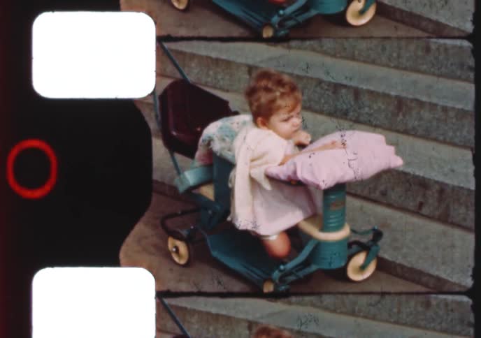 A cute baby girl sits patiently in her vintage stroller on a set of wide stone steps in this home movie from the 1950s