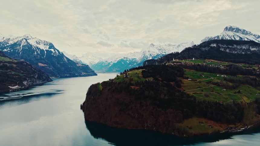 An epic aerial view captures a serene alpine lake winding between majestic snow-capped mountains and lush green hills