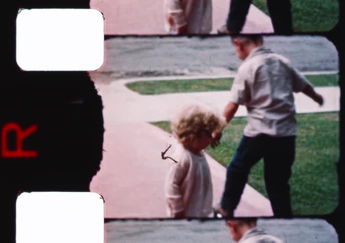 Vintage footage shows a young boy with old-fashioned roller skates learning to balance and skate on the sidewalk