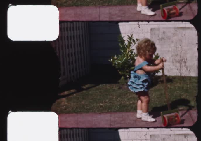 A sweet toddler in a blue ruffled outfit learns to walk with a push toy in the backyard on a sunny day