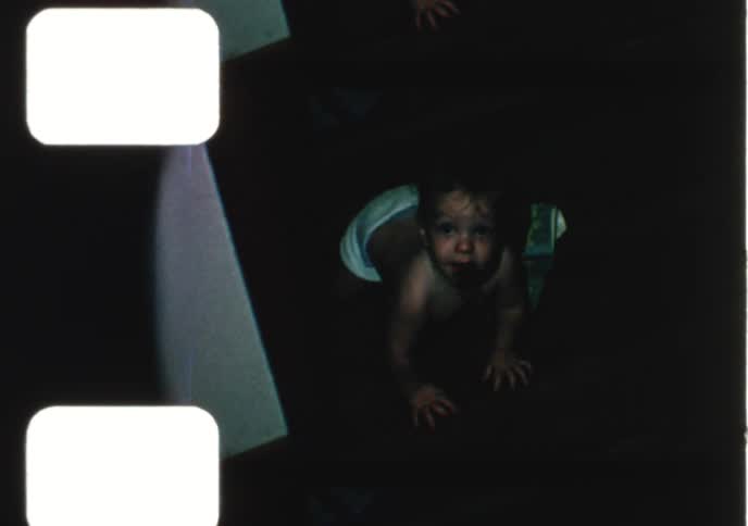 A 1960s home movie montage shows a happy baby boy in his crib, playing with a dishwasher, and crawling on the floor