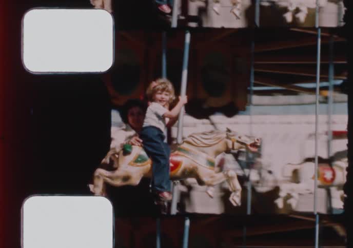 Vintage 8mm footage shows a mother and her two young children smiling and having fun on a classic carousel ride at a fair