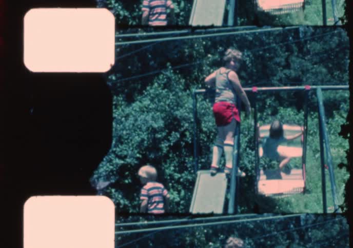 Children play together on a backyard swing set on a sunny day in this nostalgic home movie footage