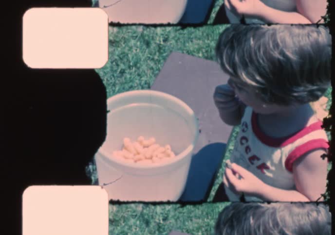 A nostalgic 8mm home movie shows a happy young boy playing on a backyard swing set and eating snacks on a summer day