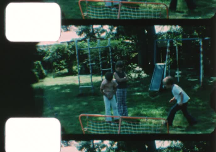 Vintage home movie footage captures three young boys playing with a ball in a backyard on a sunny day