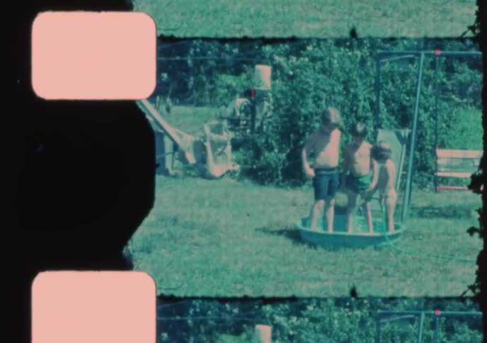 Nostalgic vintage 8mm film shows a group of young boys playing together in a small kiddie pool on a sunny summer day