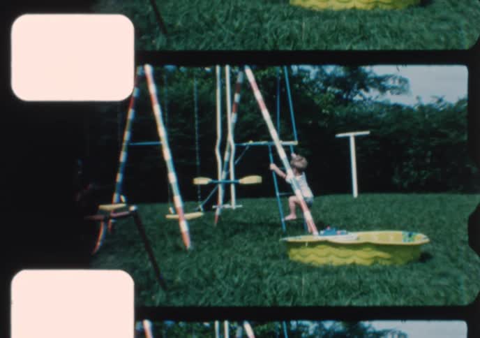 Vintage home movie footage shows a mother and her young son playing on a colorful swing set in their grassy backyard