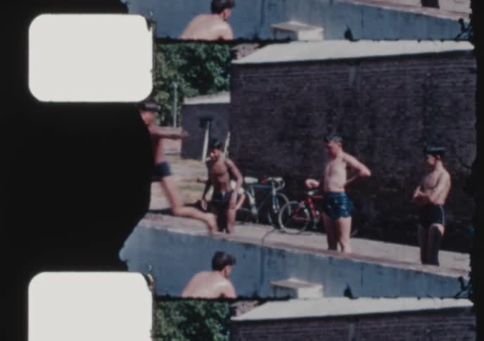Vintage 8mm film captures the nostalgic joy of a summer day as kids and a woman swim and dive into a public pool