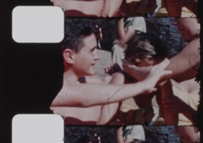 Authentic vintage 8mm film shows a group of carefree teenagers laughing and having fun together in the summer sun