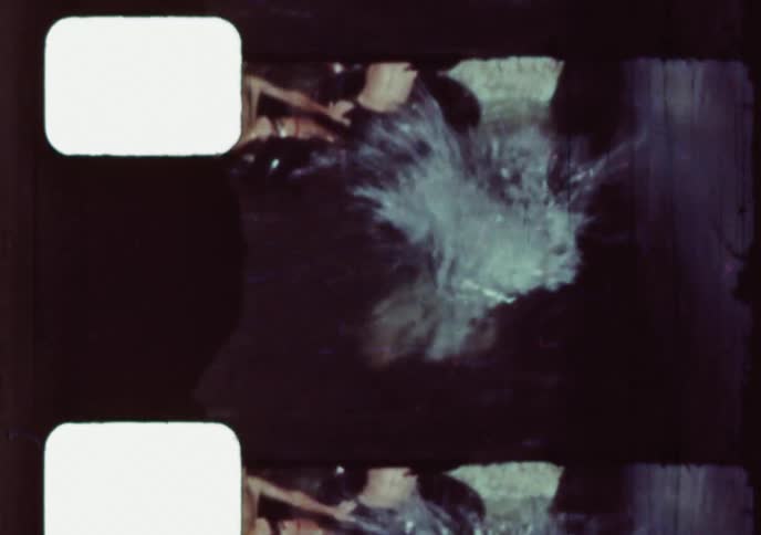 A young boy wearing flippers dives into a swimming pool on a summer day in this vintage 8mm home movie