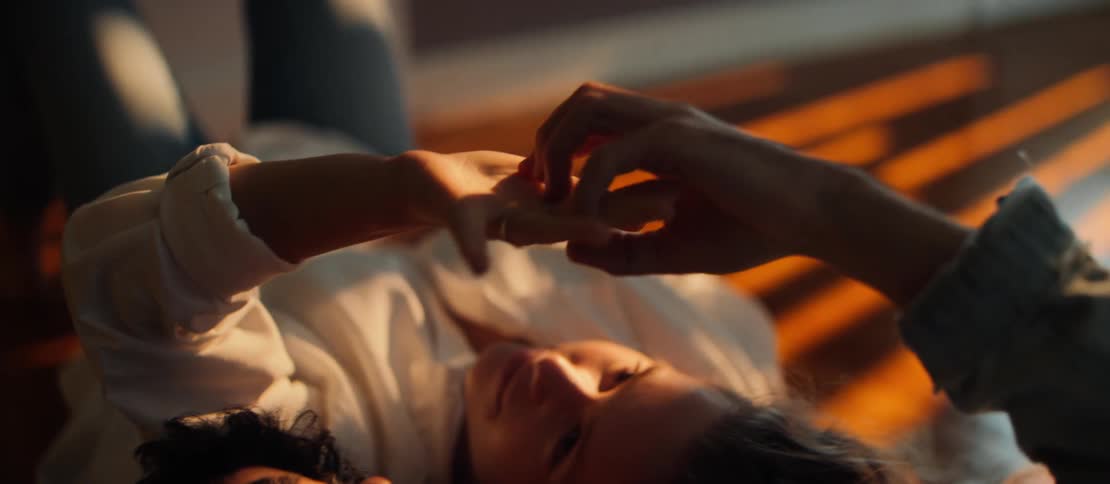 An intimate close-up of a couple tenderly holding hands while lying on the floor in the warm glow of golden hour light