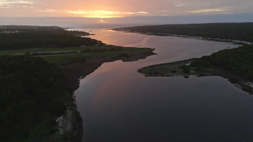 An aerial view tilts up to reveal a gorgeous sunset over a tranquil river surrounded by lush green forests