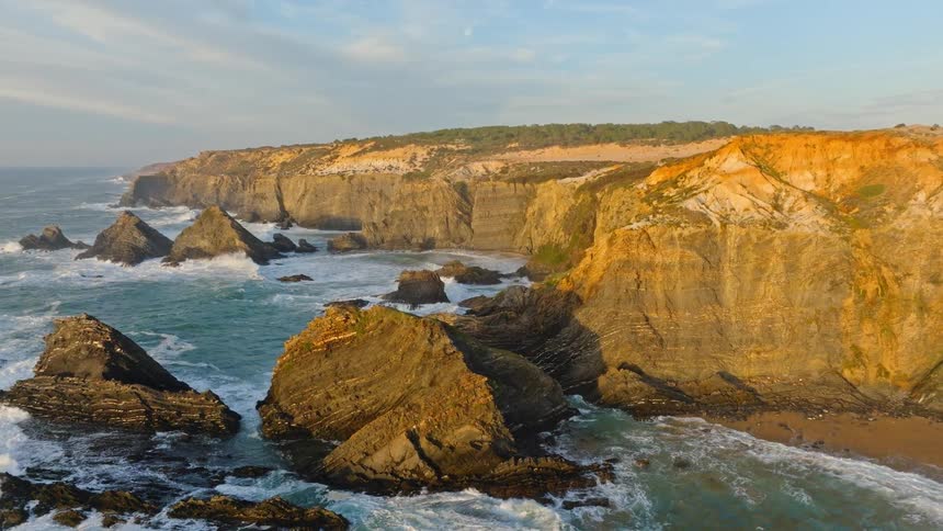 An awe-inspiring aerial view captures the dramatic cliffs and rugged coastline glowing in the warm light of golden hour as waves crash below