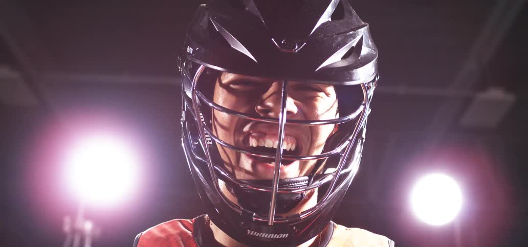 Intense close-up of a lacrosse player in a helmet laughing under dramatic lighting with a bright flash effect
