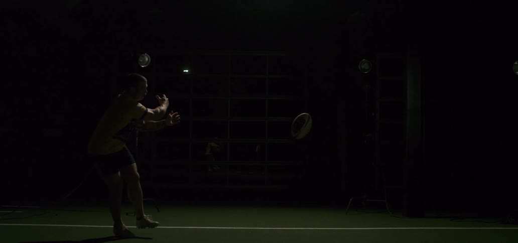 A male rugby player passes the ball in dramatic slow motion, illuminated by a flash of light in a dark studio