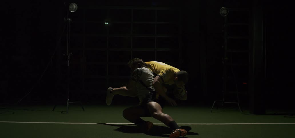 A rugby player tackles an opponent carrying the ball, bringing him down in slow motion under dramatic lighting